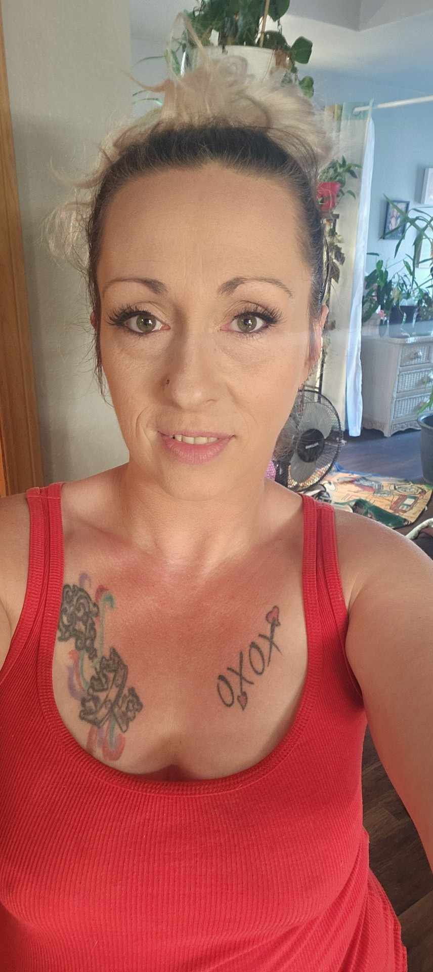 A woman with a tattoo on her chest is taking a selfie.