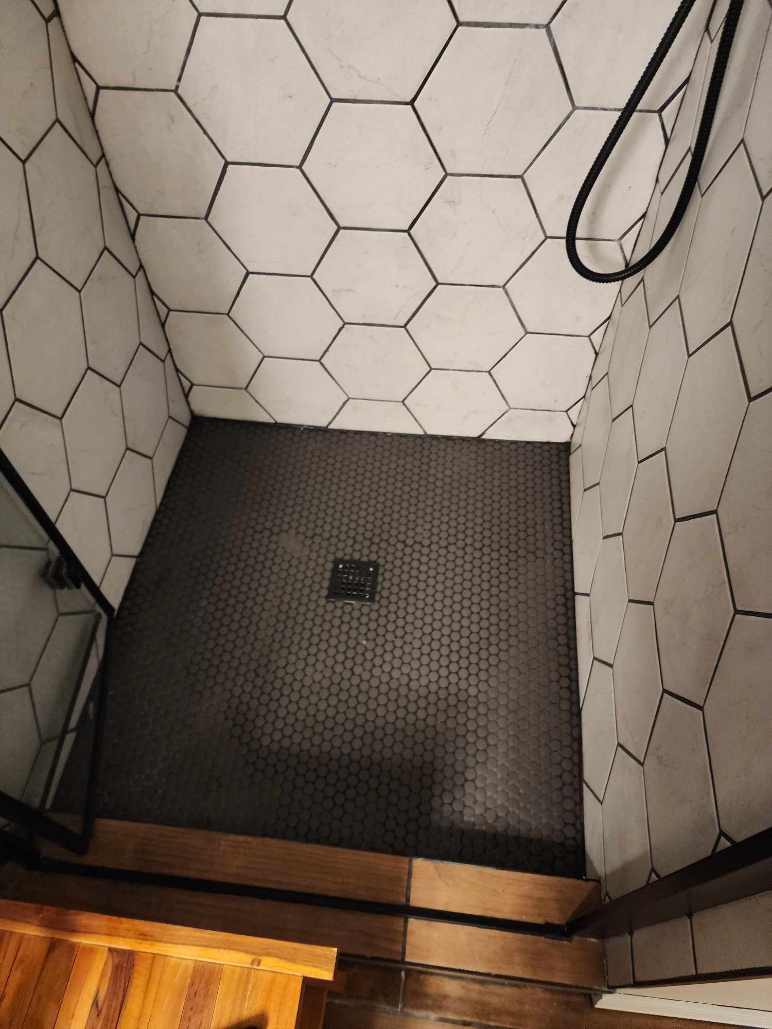 A shower with a black tile floor and white tiles on the walls.