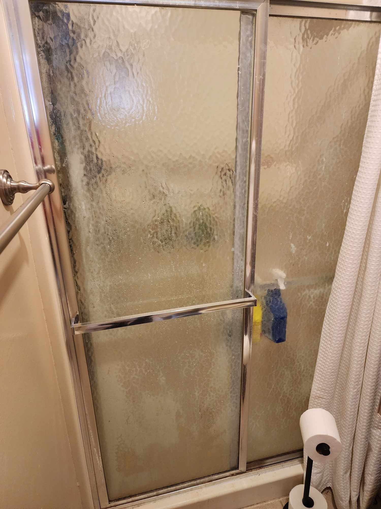 A bathroom with a sliding glass shower door and a toilet paper roll.