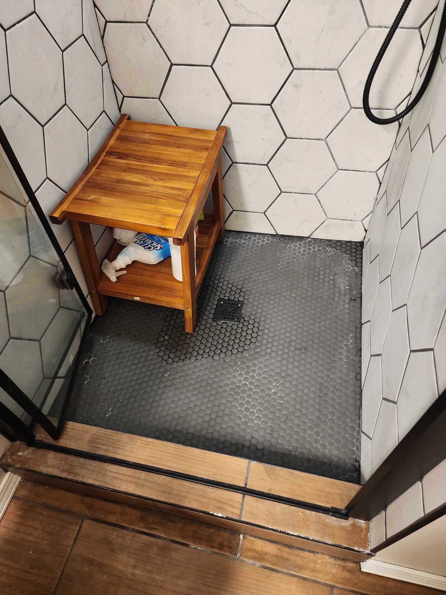 A shower stall with a wooden stool in it.