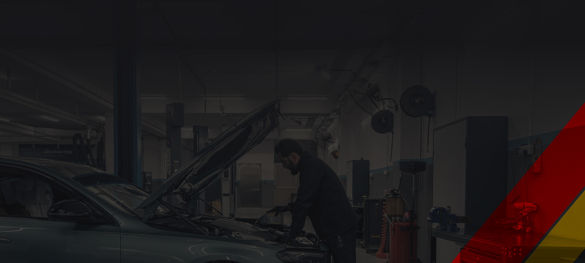 Dim auto repair shop with a car on a lift, mechanic, and red-yellow diagonal stripe on the right. | D&D Tire & Auto Center