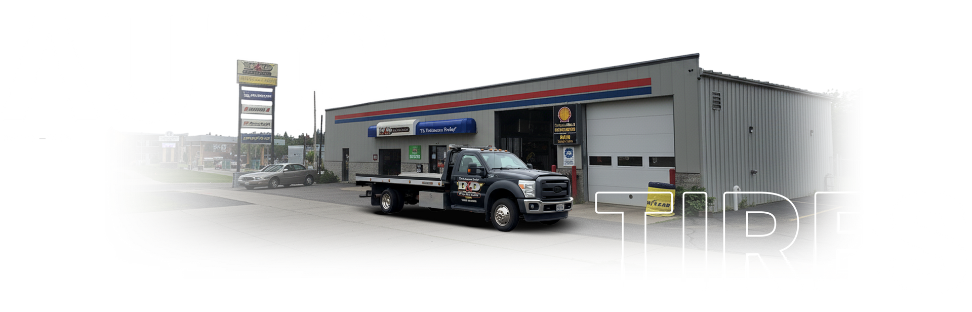 Truck parked outside an auto repair shop with open garage doors and a roadside sign