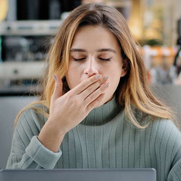 A woman is covering her mouth with her hand while using a laptop computer representing Chronic Fatigue Syndrome (CFS) Complementary and Integrative Medical Care by Salerno Wellness in Manhattan, NY, and Connecticut 