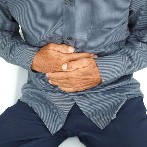 A man is sitting down with his hands on his stomach needing his Colitis and IBS IV Treatments