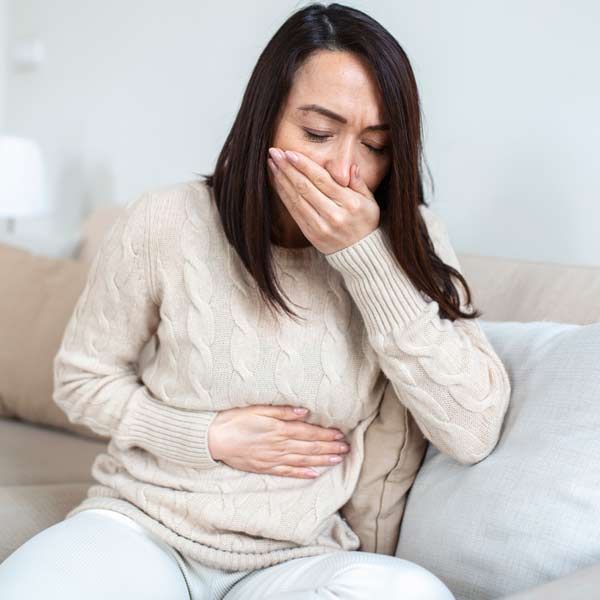 A woman is sitting on a couch, covering her mouth with her hand, needing Gastritis Treatments
