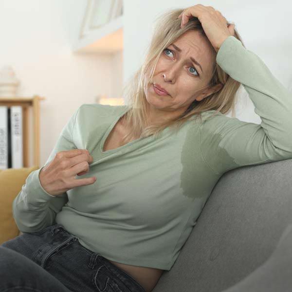 Woman on couch with sweat stains on shirt, looking distressed.