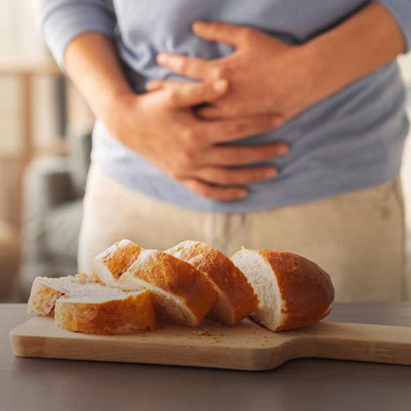 Person holding stomach near sliced bread on a cutting board, suggesting digestive discomfort.