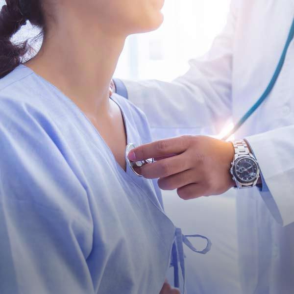 Doctor using a stethoscope on a patient's chest in a medical setting.