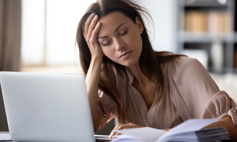 A woman is sitting at a desk with a laptop and papers with severe fatigue reading How to Remove Heav