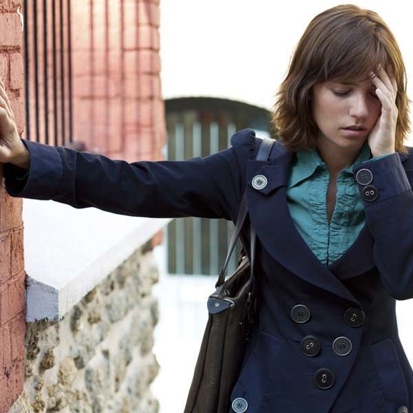 A woman leaning against a brick wall, having trouble with coordination because of Huntington's Disease