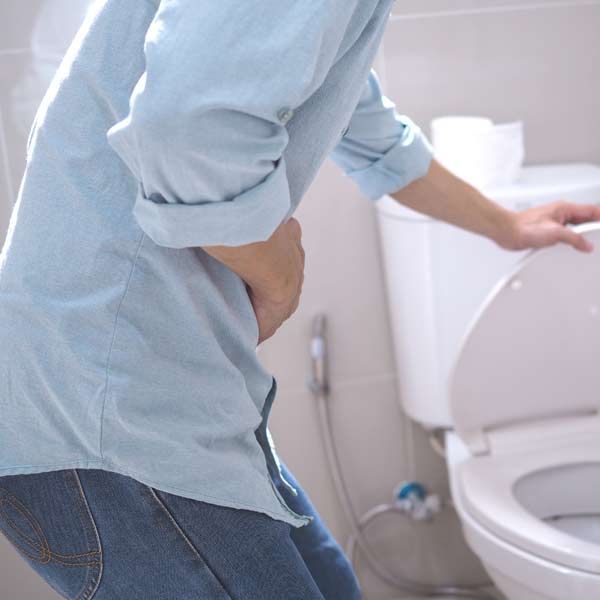 Person with IBD clutching abdomen near a toilet, possibly in pain, in a bathroom.
