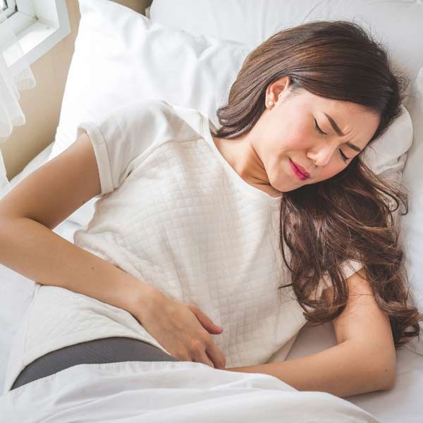 A woman is lying in bed with her hands on her stomach, needing Inflammatory Bowel Disease (IBD) Treatments