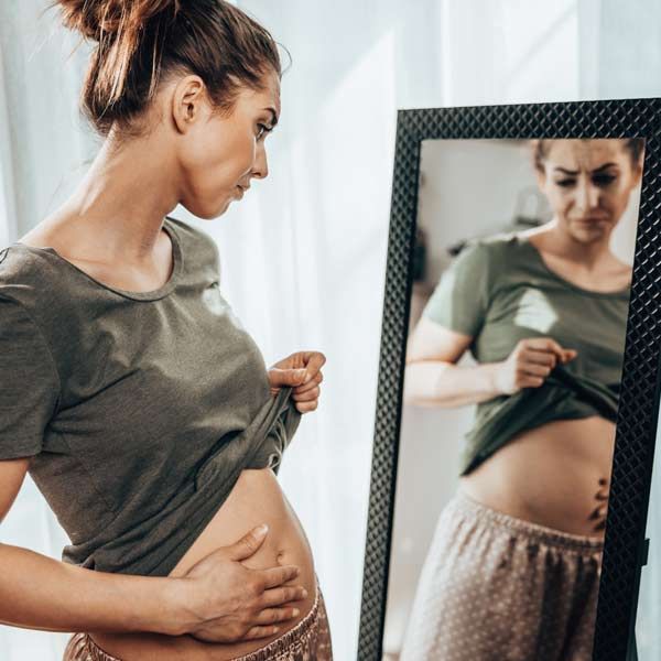 A woman is looking at her stomach in a mirror for Irritable Bowel Syndrome Treatments