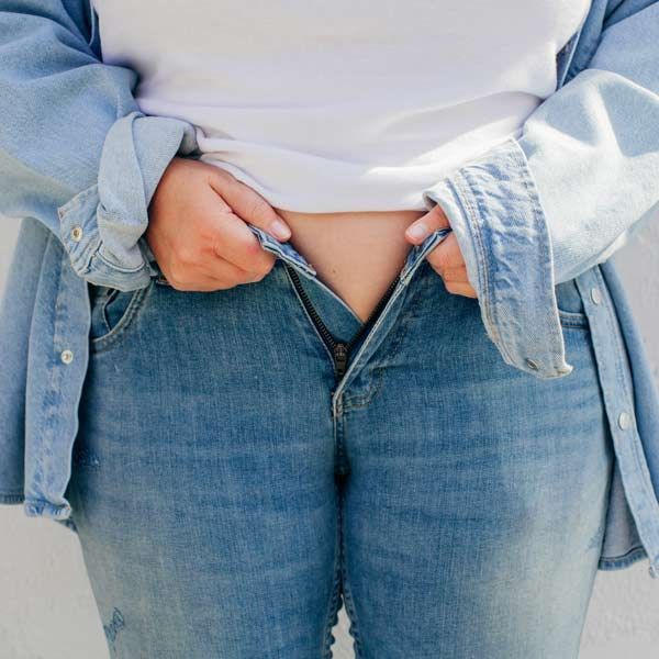 A woman wearing a white shirt and blue jeans that are too tight from sudden weight gain needs Comprehensive Integrative and Functional Medical Treatments for PCOS at Salerno Wellness in Manhattan, NYC, and Connecticut