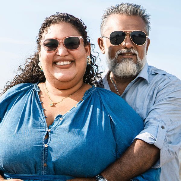 Smiling overweight couple in sunglasses outdoors, with ocean and sky in the background ready to start a resistance weight loss treatment program