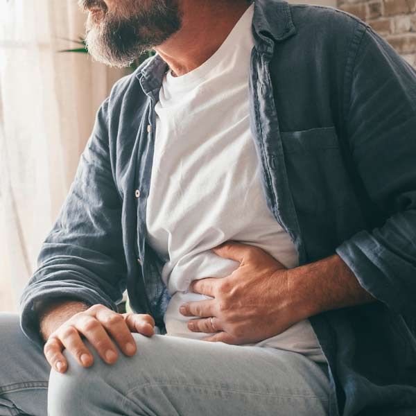 A man is sitting on a couch holding his stomach in pain indicating Short Bowel Syndrome Treatments