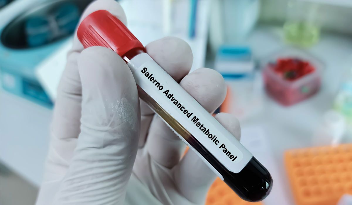 Gloved hand holding a labeled blood sample tube in a lab setting that says Salerno Advanced Metabolic Panel