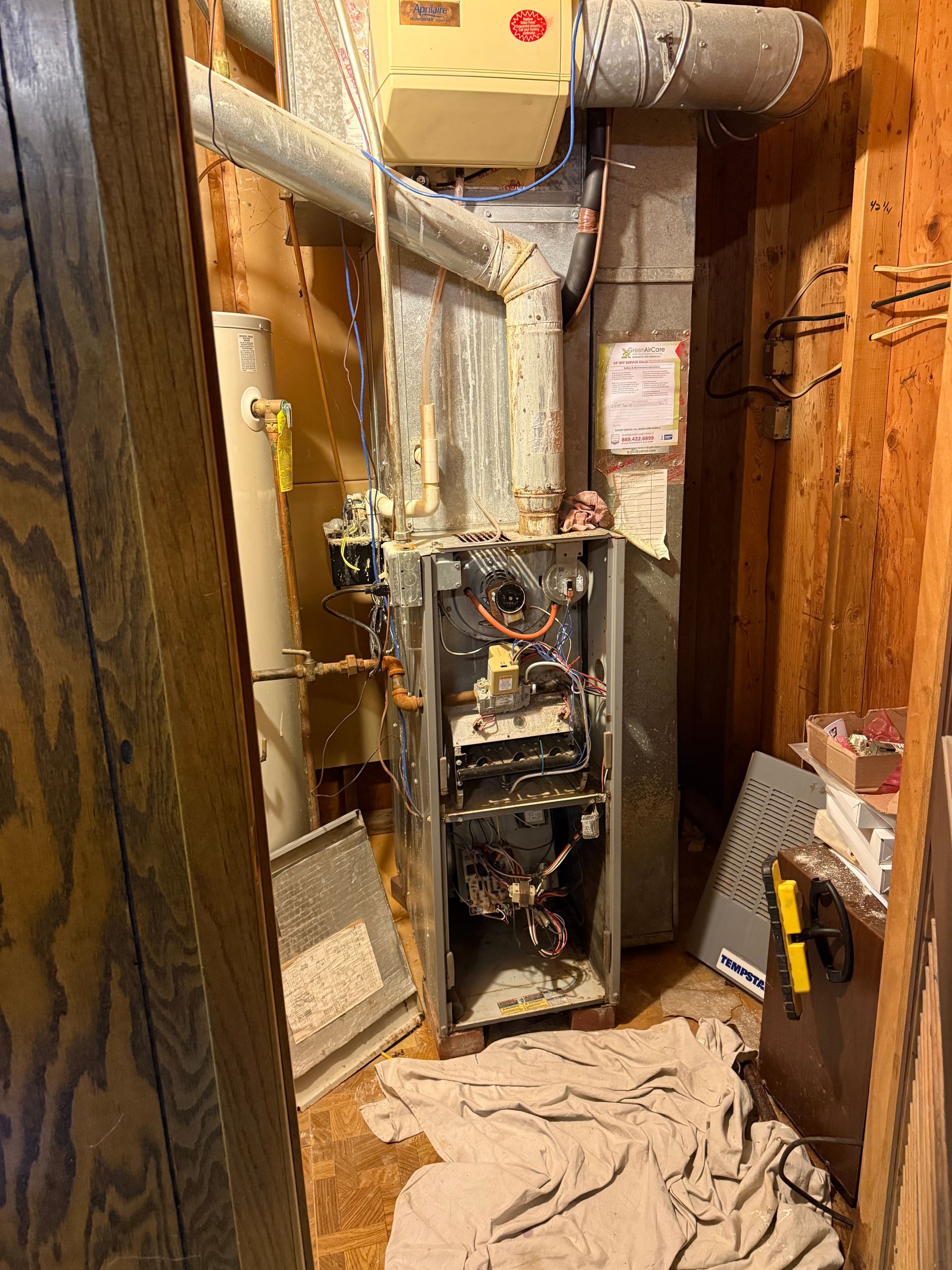 Open furnace and HVAC ducts in a cramped utility closet with a towel on the floor.