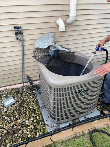 Outdoor HVAC unit being cleaned with a hose beside a house.