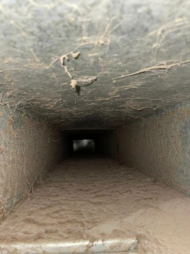 Long, dark concrete tunnel with rough ceiling and sandy floor, receding into darkness