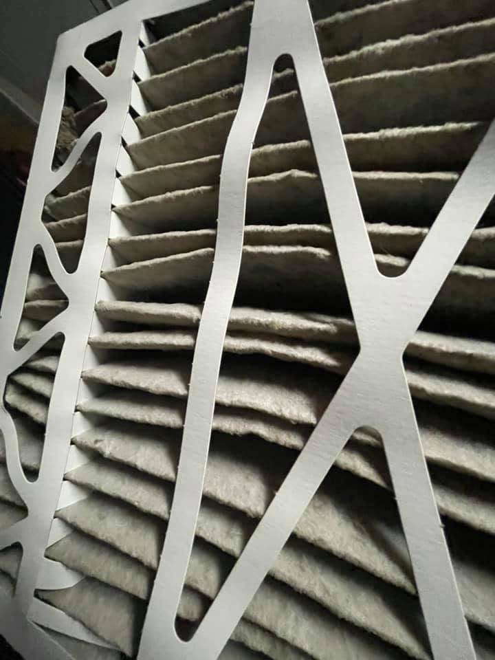 White geometric metal grille in front of a dusty beige louvered vent or wall panel