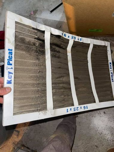 Hand holding a white pleated HVAC filter with blue labeling in a workshop setting