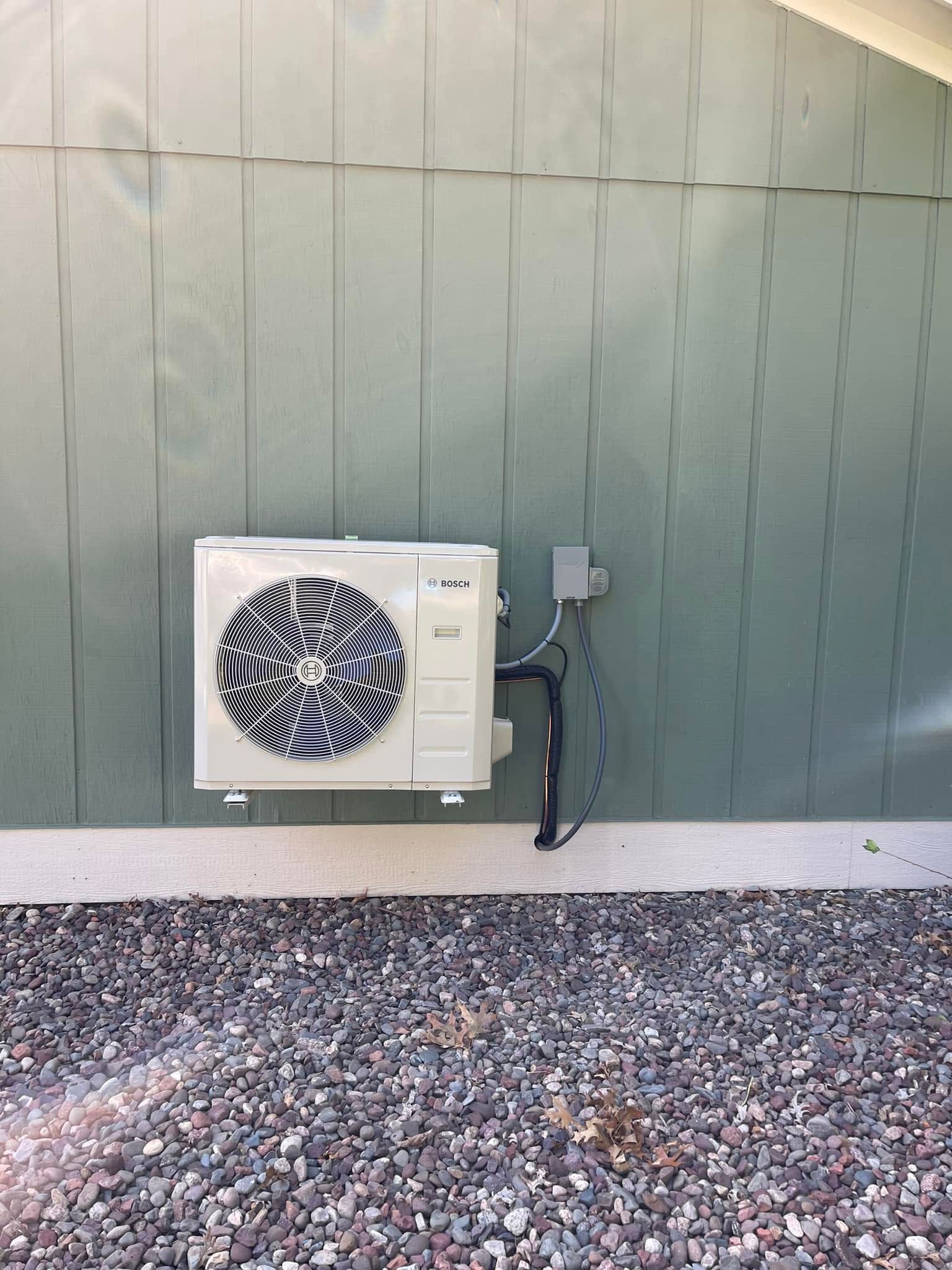 Wall-mounted air conditioner unit on a green exterior wall above gravel.