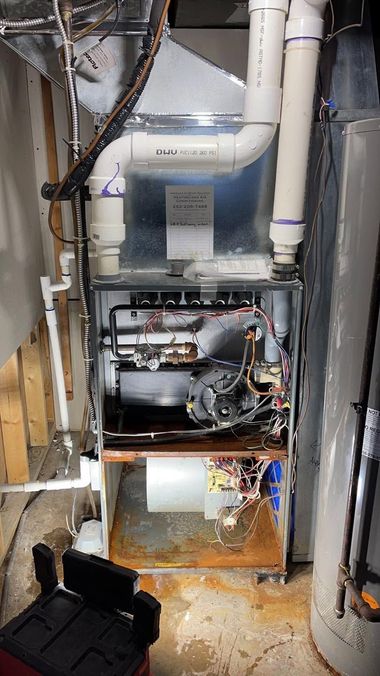 Open furnace or HVAC unit in a cramped utility space with exposed pipes and wiring