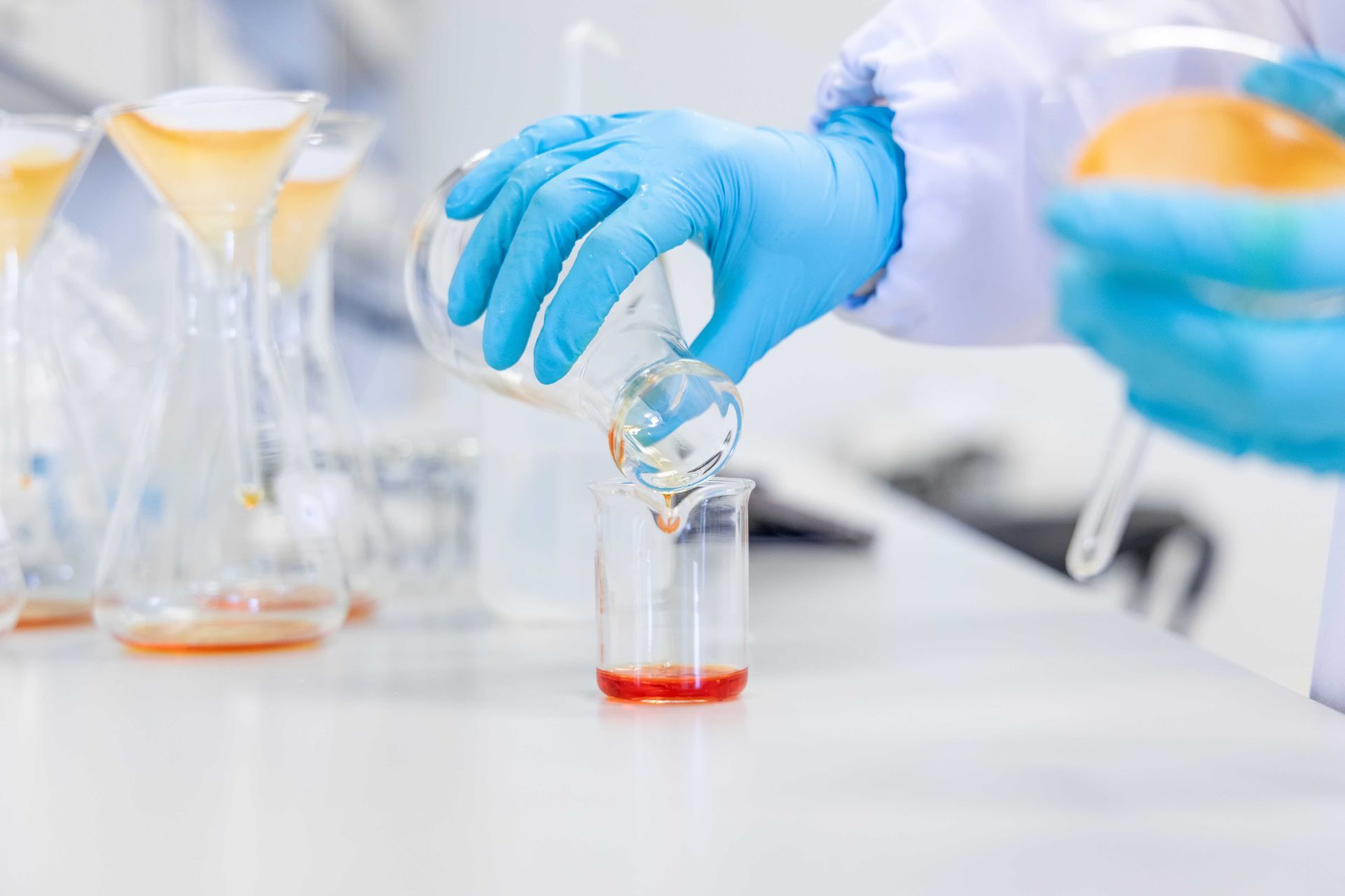 Un scientifique portant des gants bleus transvase un liquide d'un bécher dans un autre, dans un laboratoire.