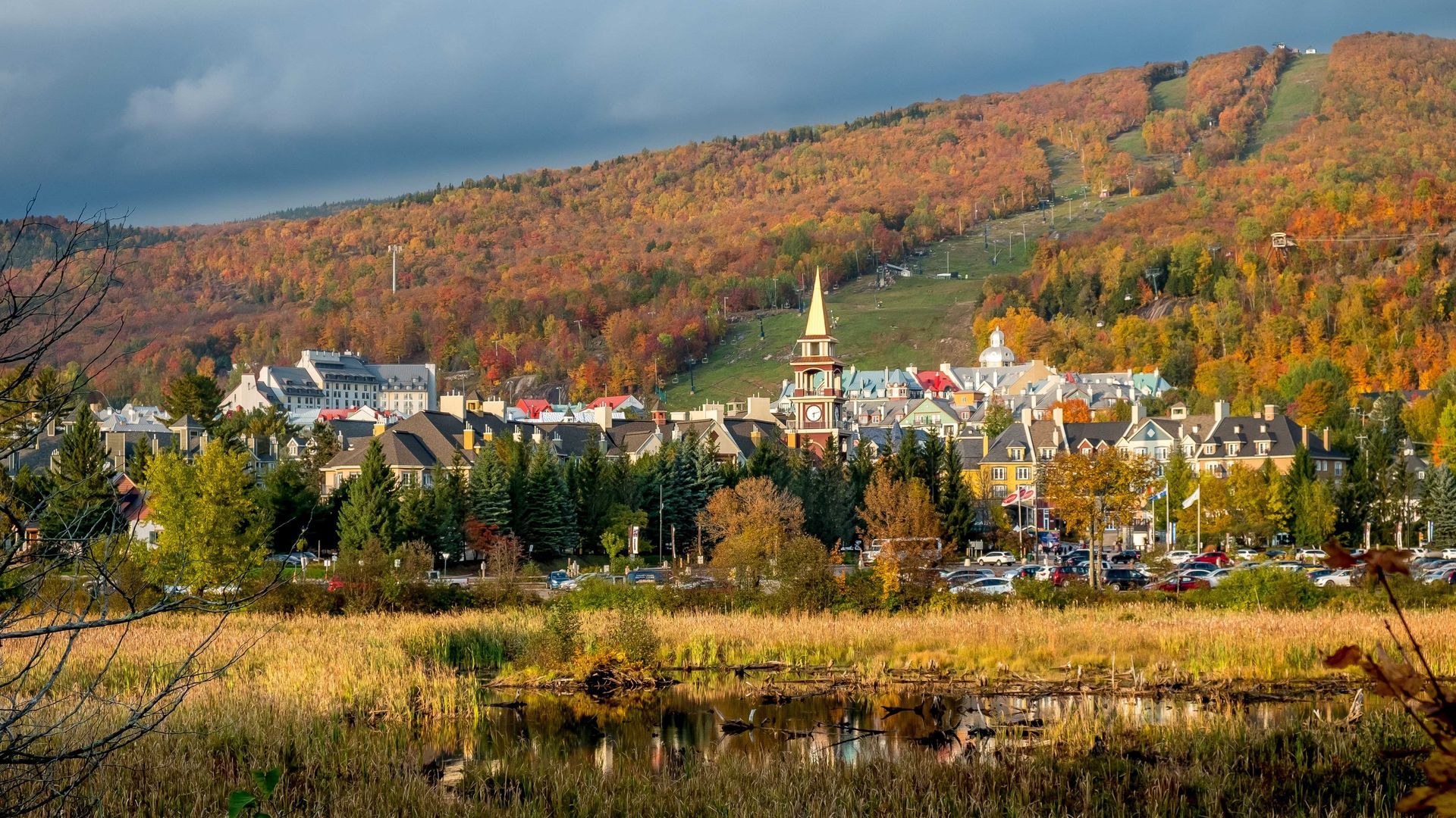 Le feuillage d'automne entoure un village niché au pied d'une montagne, avec un clocher d'église.