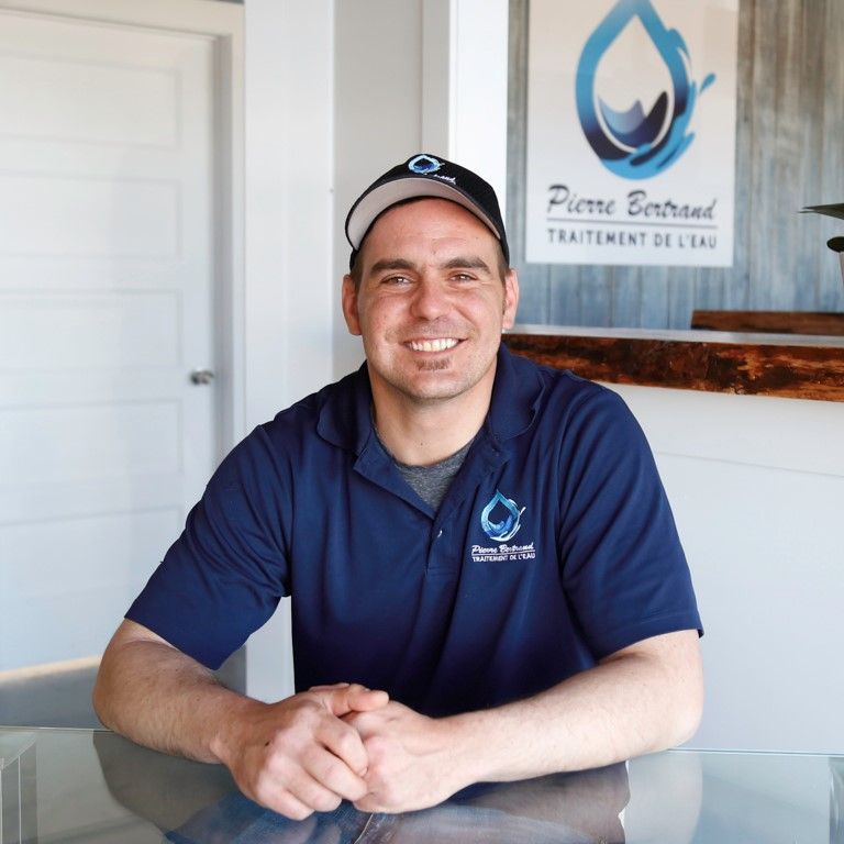 Un homme portant une casquette et un polo sourit devant le logo d'une entreprise de traitement des eaux.