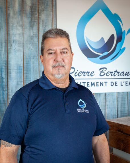 Un homme en chemise bleue se tient devant un logo orné d'une goutte d'eau.