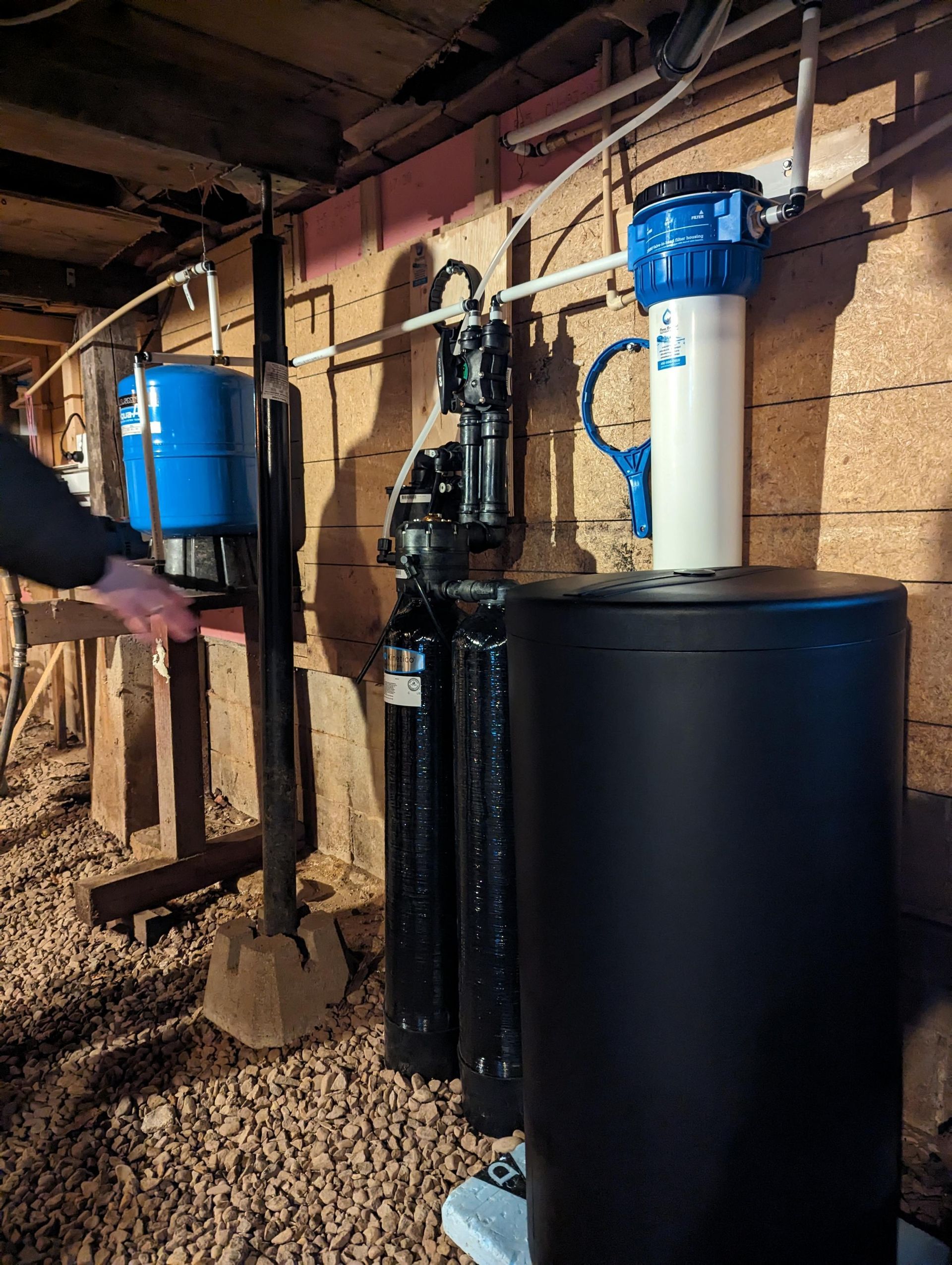 Système de filtration d'eau installé dans un sous-sol, avec divers réservoirs, tuyaux et une main tendue vers celui-ci.