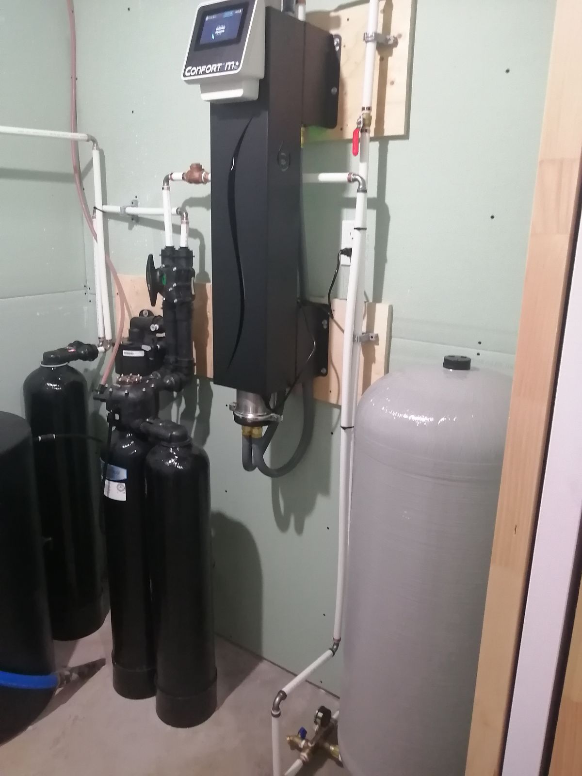 Système de filtration d'eau avec divers réservoirs, tuyaux et panneau de commande adossé à un mur dans une buanderie.