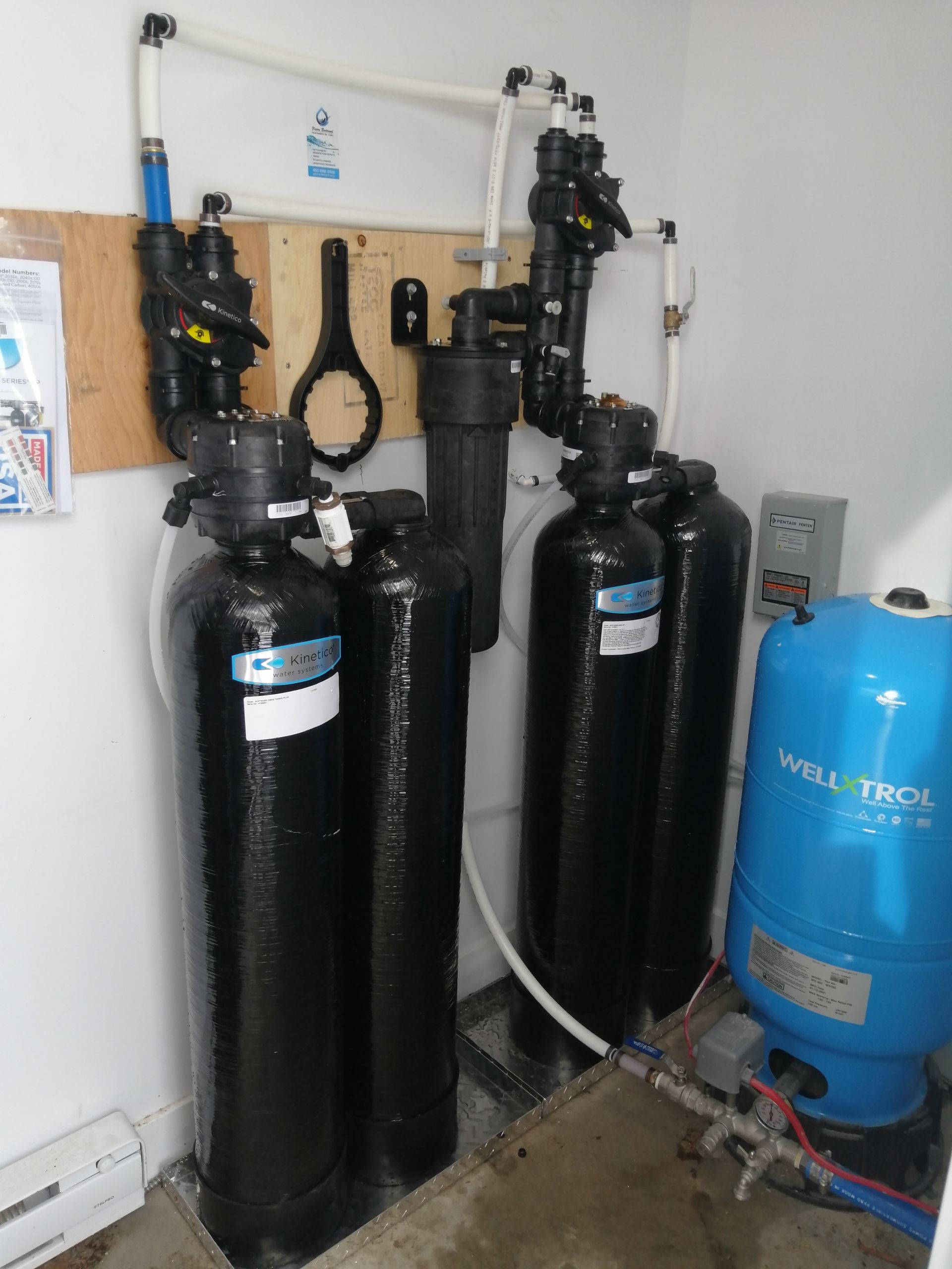 Système de filtration d'eau avec plusieurs réservoirs noirs et un réservoir sous pression bleu dans un local technique.