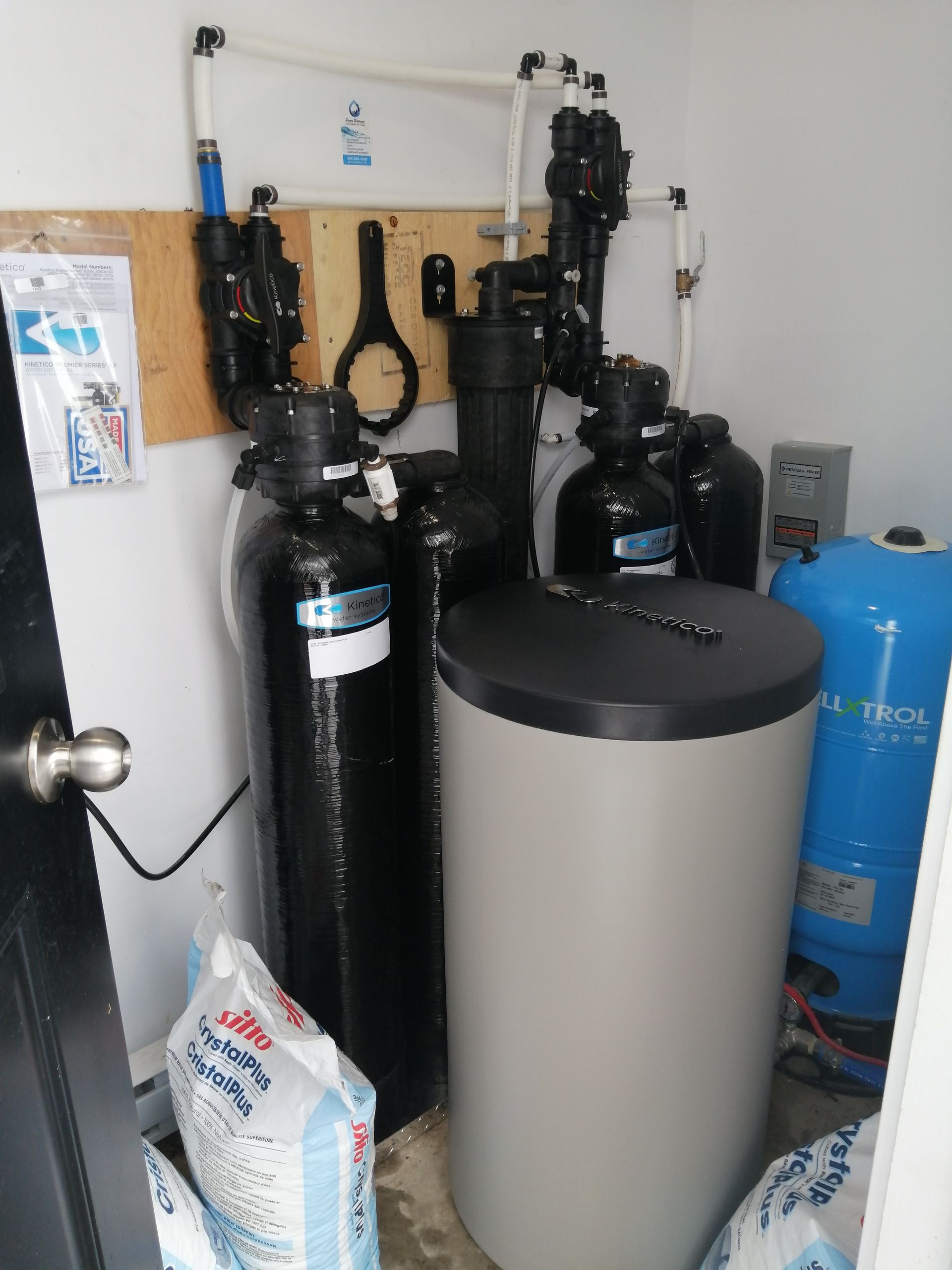 Système de filtration d'eau dans une buanderie. Réservoirs noirs, filtre gris, tuyaux blancs et réservoir d'eau bleue.