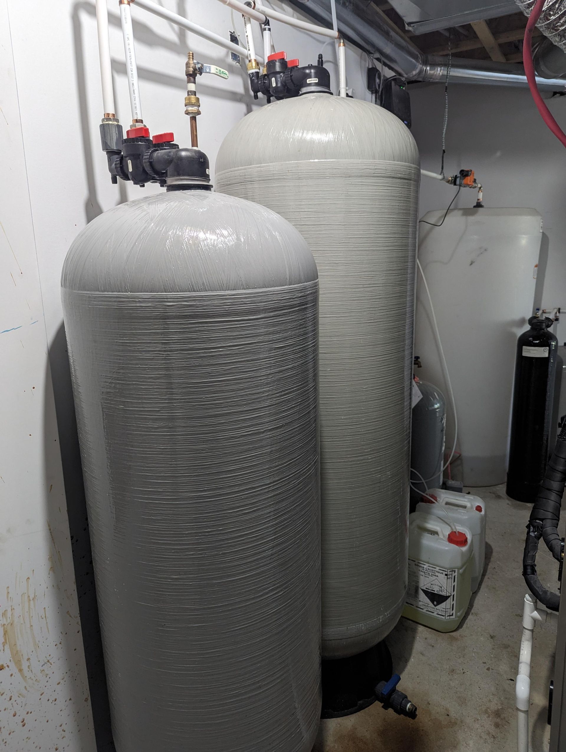 Deux grands réservoirs de filtration d'eau avec tuyaux et vannes raccordés dans une buanderie.