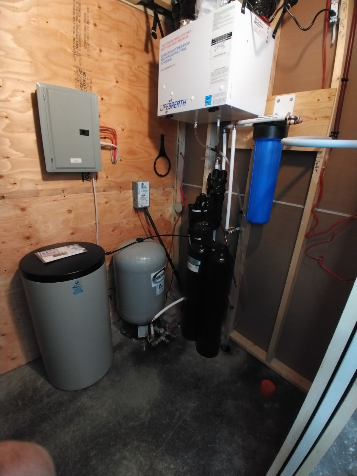 Système de filtration d'eau et réservoir dans une buanderie. Équipements gris et noirs fixés sur des panneaux de bois.