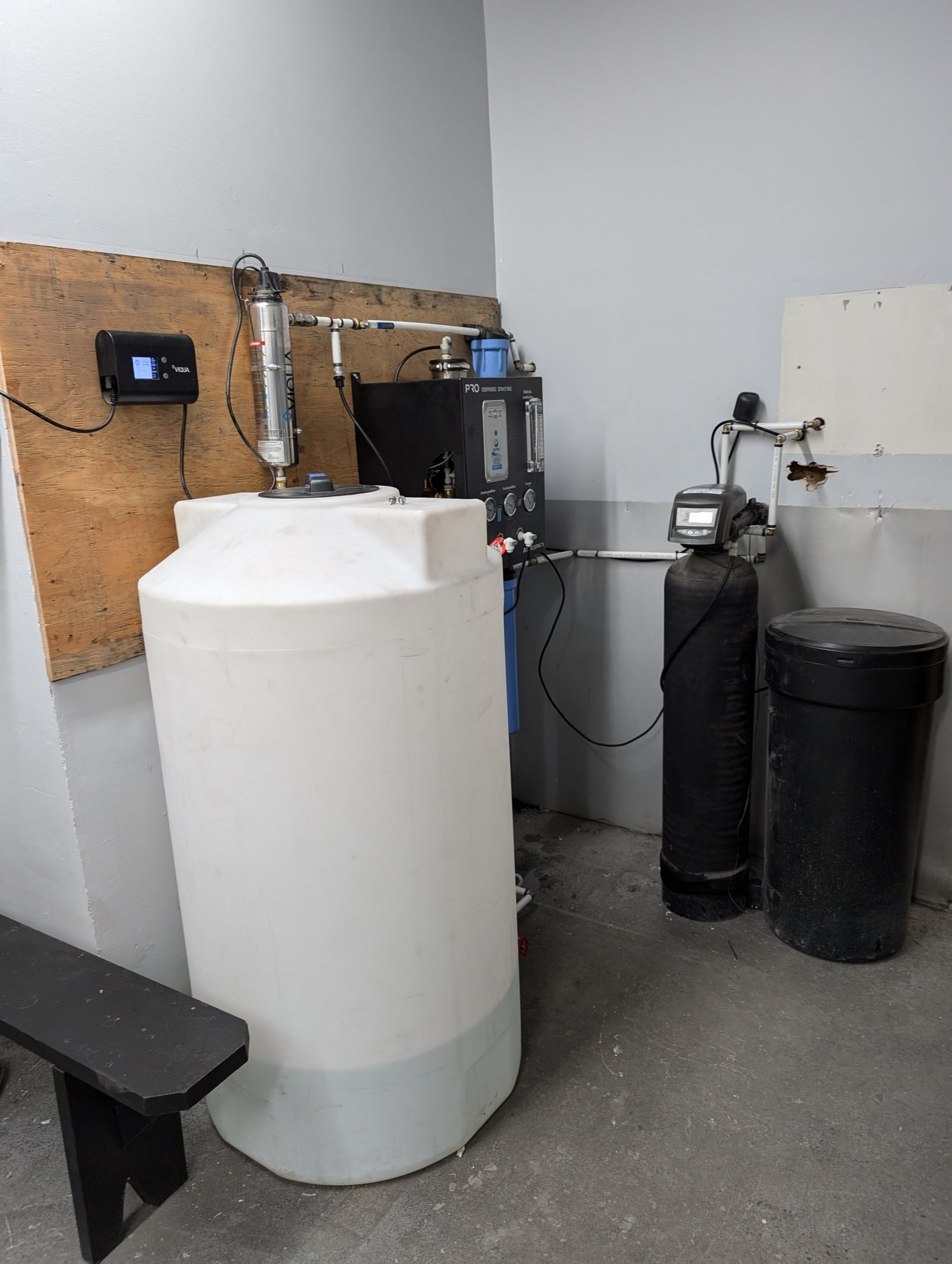 Système de filtration d'eau avec réservoir blanc, équipements noirs et murs gris dans une buanderie.