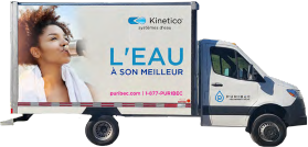 Un camion-citerne aux couleurs de la marque. Une femme boit à une fontaine à eau. On peut lire « L'eau à son meilleur » sur le côté.