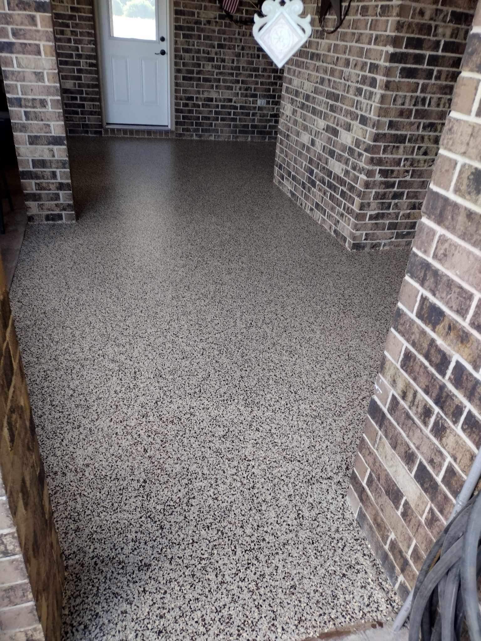 Speckled concrete porch floor between brick walls, with a white front door in the background