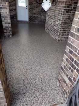 Brick porch with speckled concrete floor and a white door at the back.