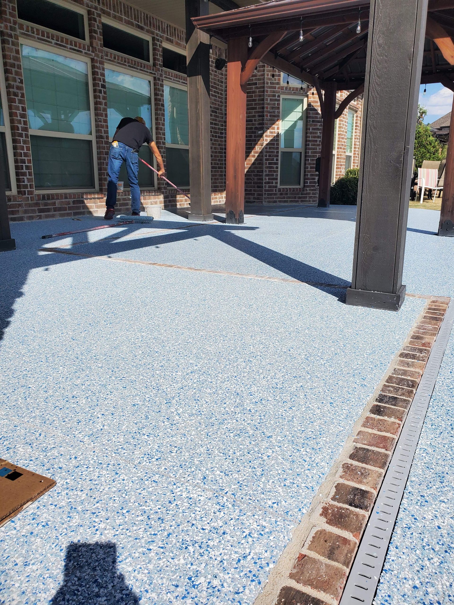 Worker spraying blue gravel on a porch beside a brick border