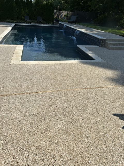 Backyard swimming pool with dark water and a light gravel deck in sunlight