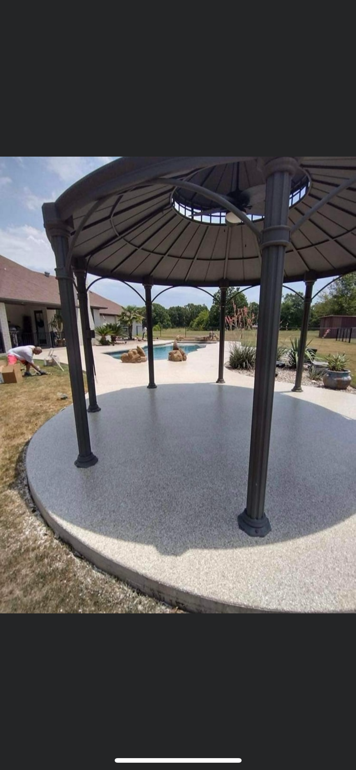 Open gazebo with a thatched roof on a gravel pad in a sunny park.