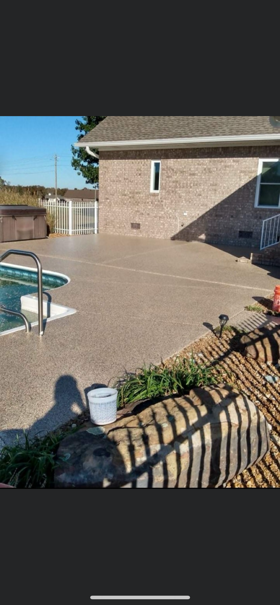 Backyard patio with a swimming pool, brick house, and a fence in bright sunlight