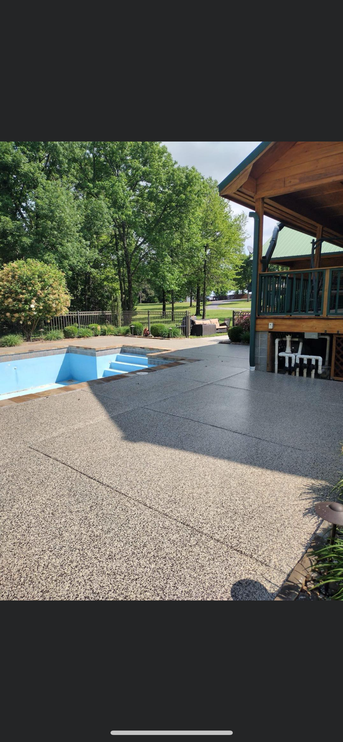 Backyard pool beside a gravel patio and covered deck under green trees