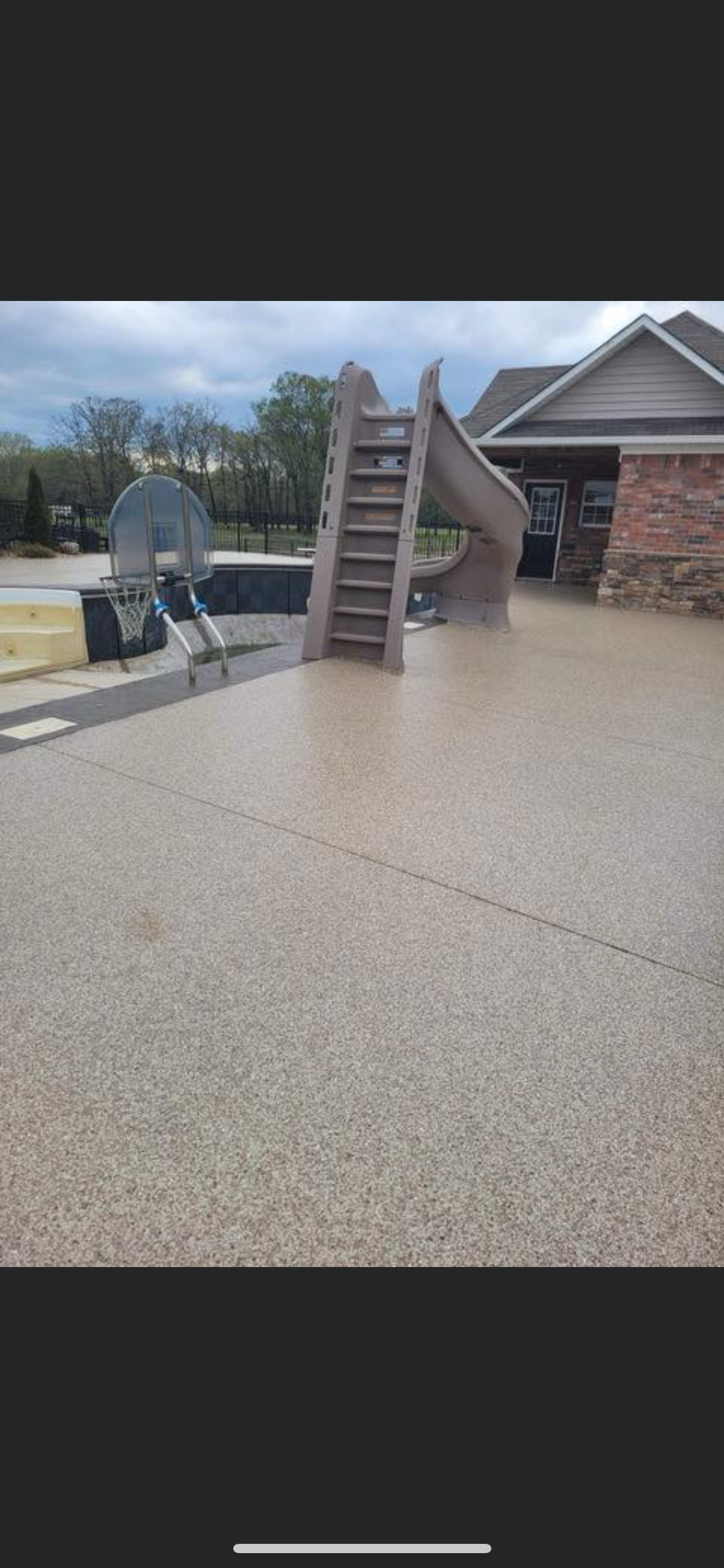 Playground with a ladder and slide on a concrete patio beside a brick house