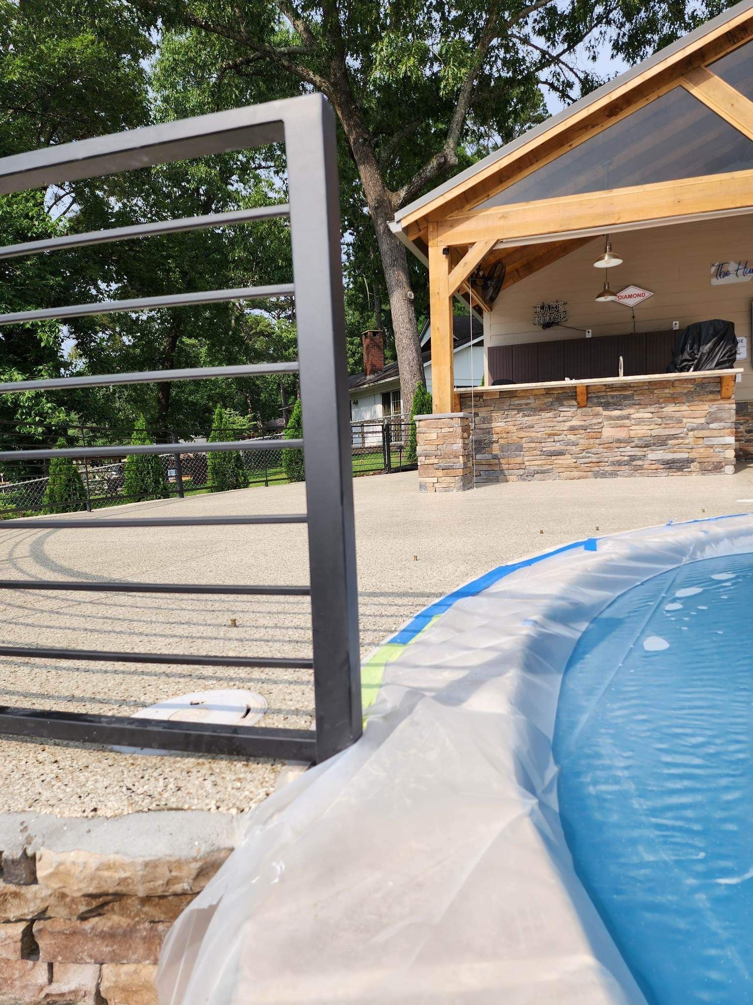 Poolside patio with a black metal gate, stone pavilion, and white pool cover in the foreground