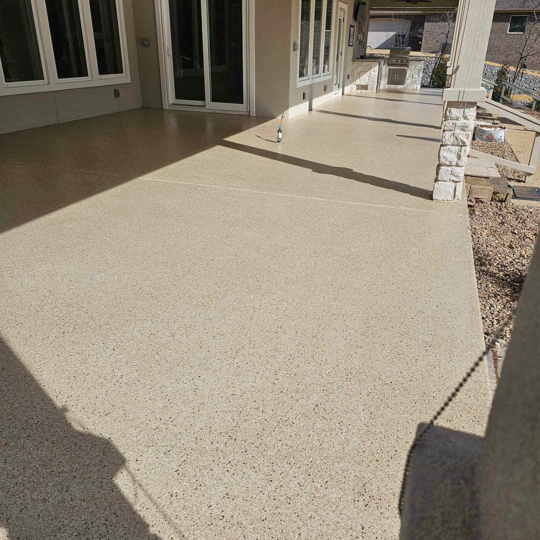 Concrete patio/walkway beside a house with sliding glass doors and stone edging in bright sunlight